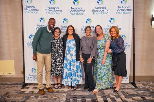 six people representing patient advocates, researchers, healthcare providers, and non-profit leaders stand for a photo in front of a National Scleroderma Foundation banner.